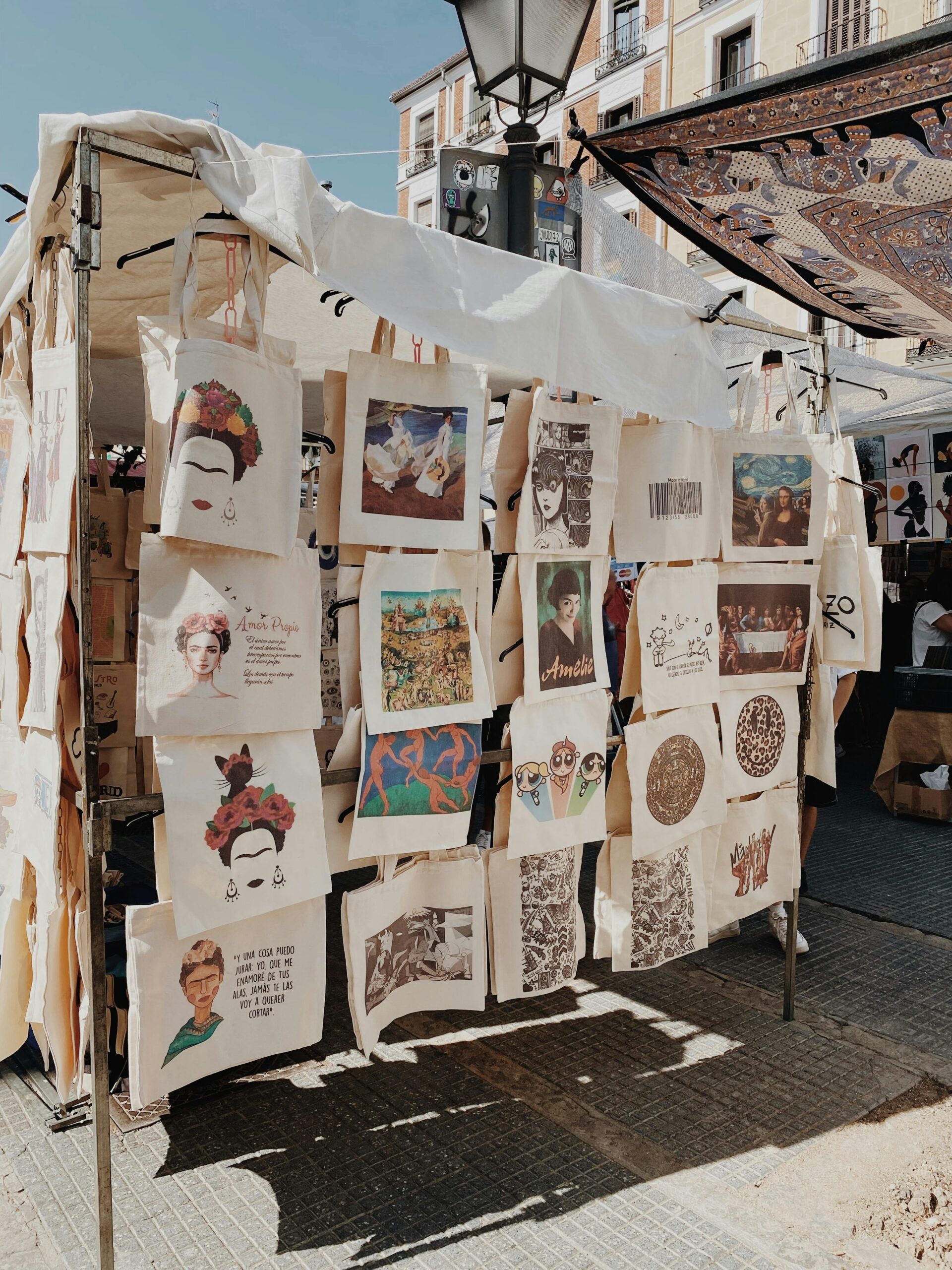 Tote bags with artistic designs displayed at an outdoor market, showcasing vibrant art for sale.